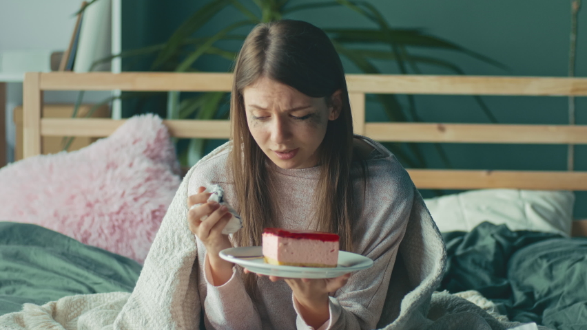 Heartbroken Girl Sitting on Sofa, Crying, Eating Cake, Using Tissues. Upset Young Woman Wrapped in Blanket Worry Separation or Divorce. Difficult Period of Life Having Psychological Problems. | Shutterstock HD Video #1090777165