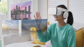 Asian people girl fun play smart VR 360 remote city tour in metaverse app look at augmented AR VFX game platform on goggles glasses headset sit at sofa couch enjoy leisure lifestyle vacation at home.