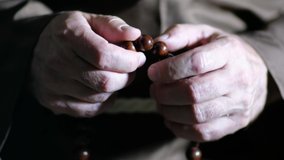 Close up video of the hands of a old monk are fingering the wooden rosary.
