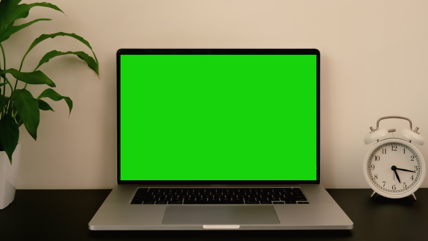 Workplace with green screen laptop computer and clock on black desk office table.