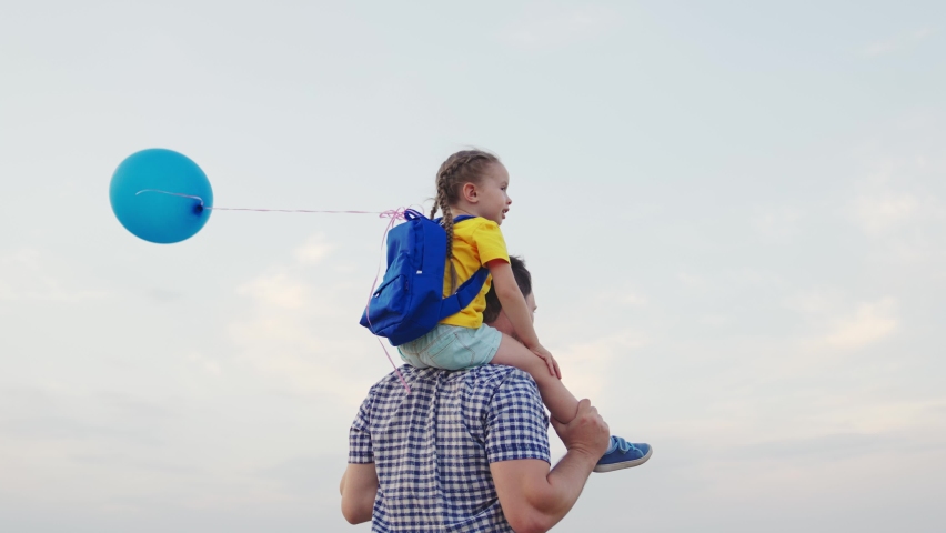 little girl sits shoulders of her dad against sky with balloon. happy family. hold gel ball with hand child kid. chidhood dream. papa day. childhood summer travel with backpack. concept happy family