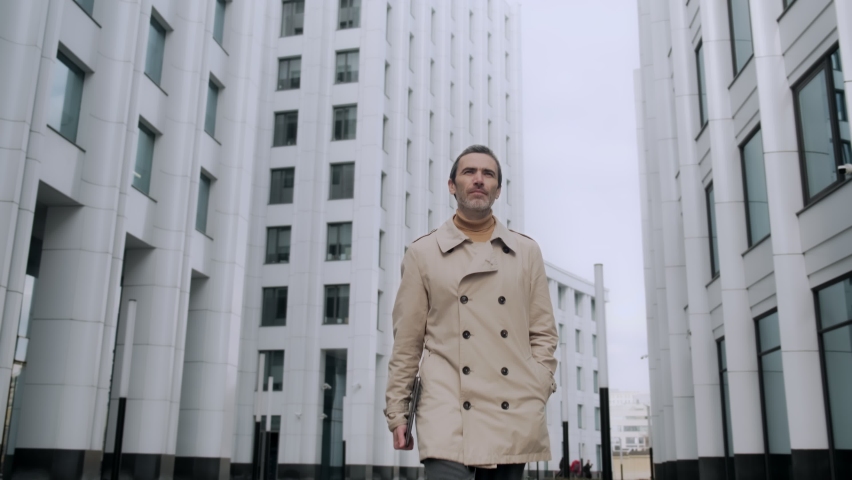 Front view of an ambitious handsome businessman walking down a city street in the city center. Stylish confident business man walks forward to the camera, picks up the phone and talks.
