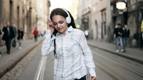 Young beautiful woman with dreadlocks listening music and dancing in the city centre. Slow motion of happy young woman in 
headphones dancing outdoors in city street.