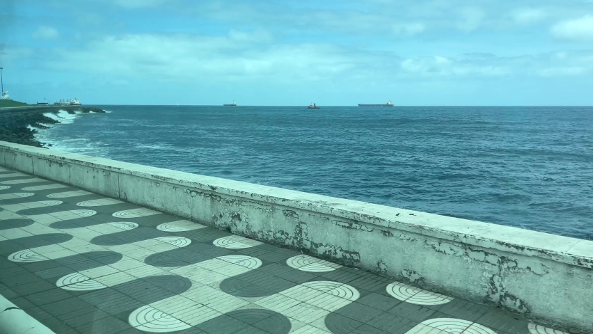 Driving by Las Palmas coast road with waves hitting the rocks and cargo ships on background in Canary Islands, Spain. Natural landscape in the city concept