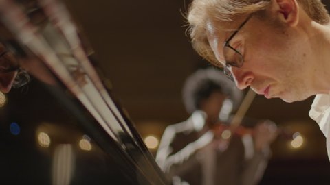 Close up handheld shot of professional musician playing grand piano with violin accompaniment on stage