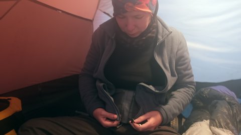 A girl in a tent sits and puts on a warm fleece jacket before climbing Mount Kilimanjaro