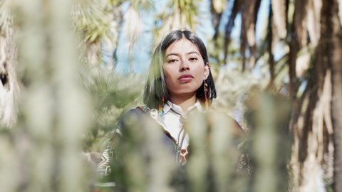 Pensive Young Native American Girl connected with nature. Beautiful Indigenous woman looking at camera through the vegetation