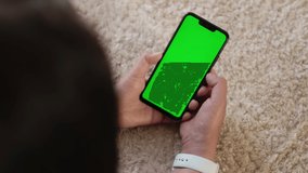 Phone with Green Screen and Chroma Key. Chromakey Mockup, Luma Keying, Cellphone in Female Hands, With No Touches and Tapping. Watching Video Content, Relax in Home, Lying on Carpet. Top View. 