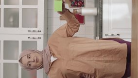 Woman in hijab is holding something green in the kitchen, showing a product, smiling. Creative 3d artists can replace the green box with any product they want.Video for the vertical story.