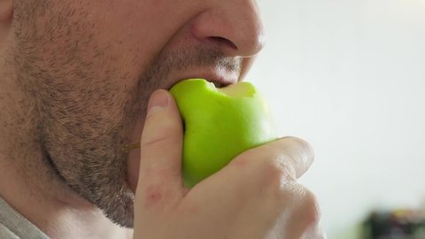 man eating green apple close up slow motion. an unshaven guy eats an apple, chews it slowly, the whole face is not visible. young man mouth eating an apple. fruit light snack.