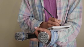 A girl with microphones in her hands writes news in a notebook. Interview. The journalist is working. the reporter. Media. Pencil in hand. Notebook entries. Journalist in a plaid shirt. 4k