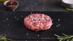 Strewing pepper on raw beef burger patty on dark background. Cooking concept. 4k video