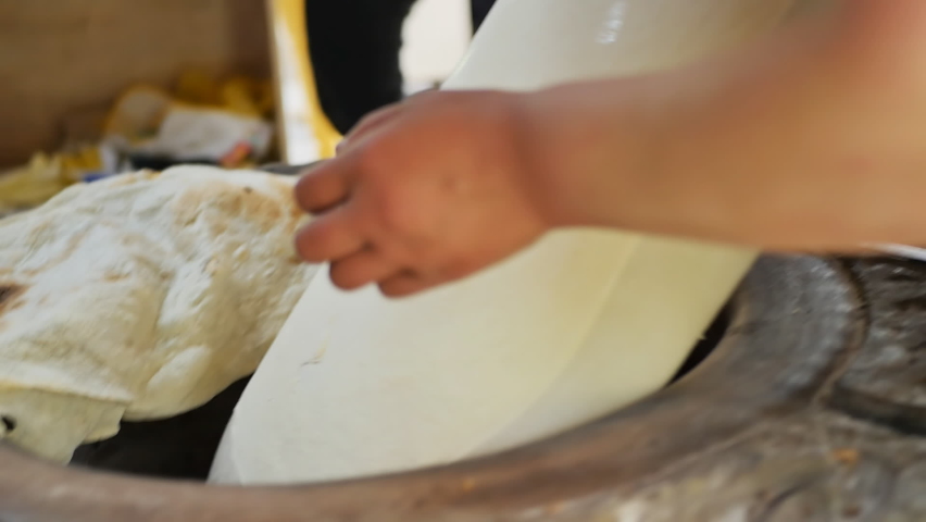 woman national baker bakes Armenian lavash in tandoor. He lowers the jigging pad with the dough into the tonir and sticks the dough to the hot stone with a sharp movement of the hand. Royalty-Free Stock Footage #1090801795