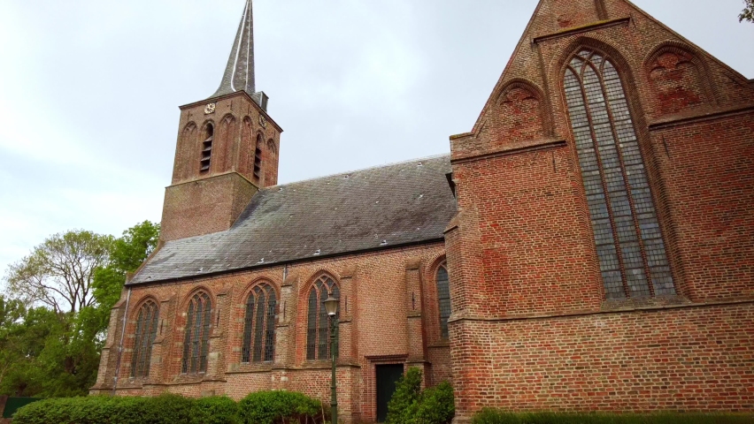 Low angle view outdoors, along a 14th century scenic Aisle Less church, church tower with beautiful Gothic stained glass windows in a small picturesque village in Schellinkhout in the Netherlands Royalty-Free Stock Footage #1090803951