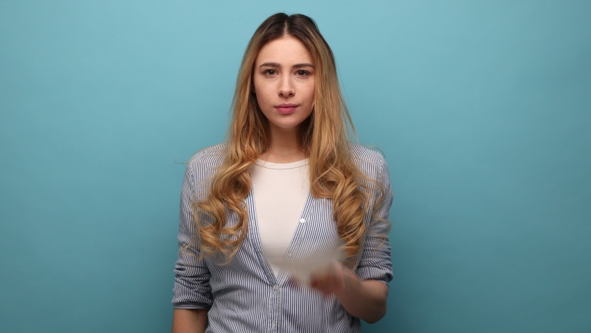 Multiple personality. Attractive woman showing different emotions, taking off mask changing facial expressions, wearing striped shirt. Indoor studio shot isolated on blue background.