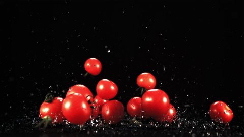 Fresh tomatoes fall with splashes of water on the table. On a black background. Filmed is slow motion 1000 fps.