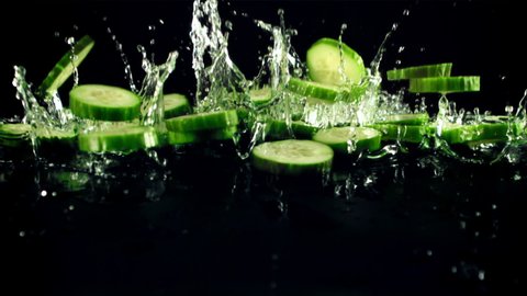 Pieces of fresh cucumbers with drops of water fly up and fall. On a black background.Filmed is slow motion 1000 fps.
