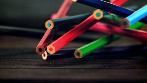Colored pencils fall on a wooden table. Against a dark background. Filmed is slow motion 1000 fps.