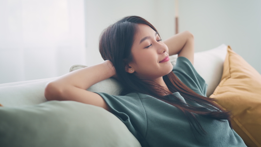 Relaxed young asian woman enjoying rest on comfortable sofa at home, calm attractive girl relaxing and breathing fresh air in home. Royalty-Free Stock Footage #1090811187