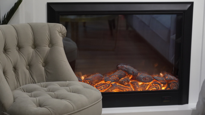 Cozy stylish armchair and electric fireplace with artificial sparkling flame, interior decor, orange flames and decorative logs. Royalty-Free Stock Footage #1090812493