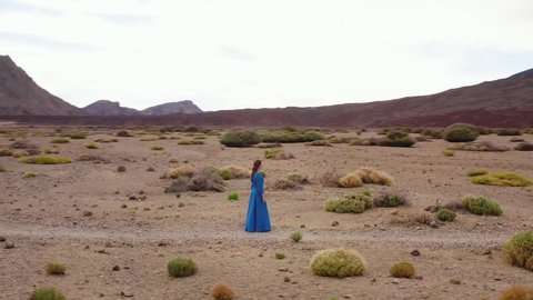 Woman in a blue dress in the middle of a landscape of hardened lava in the Teide National Park. Drone flying around a person