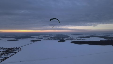 paragliding in tandem over flat fields in winter at sunset