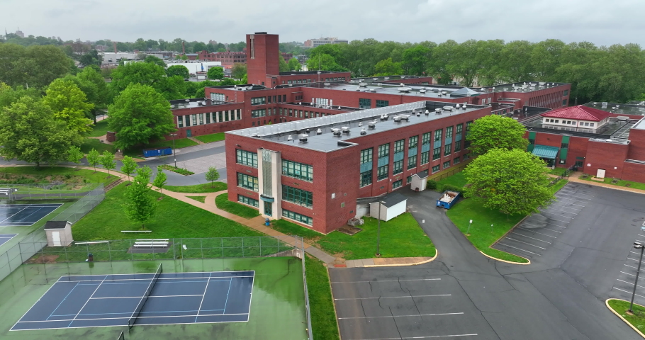 Aerial orbit around school. Rain drop falls on lens of drone. High school on wet, rainy, spring day in America. Tennis courts and classrooms. Royalty-Free Stock Footage #1090818673