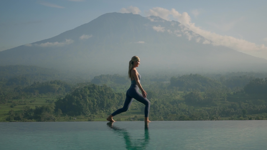Fit woman in sportswear standing in Warrior Position stretching arms above head, Mount Agung in background, bright morning sunlight Royalty-Free Stock Footage #1090820289