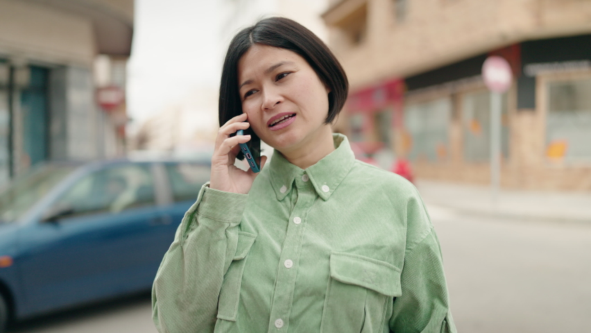 Young chinese woman smiling confident talking on the smartphone at street