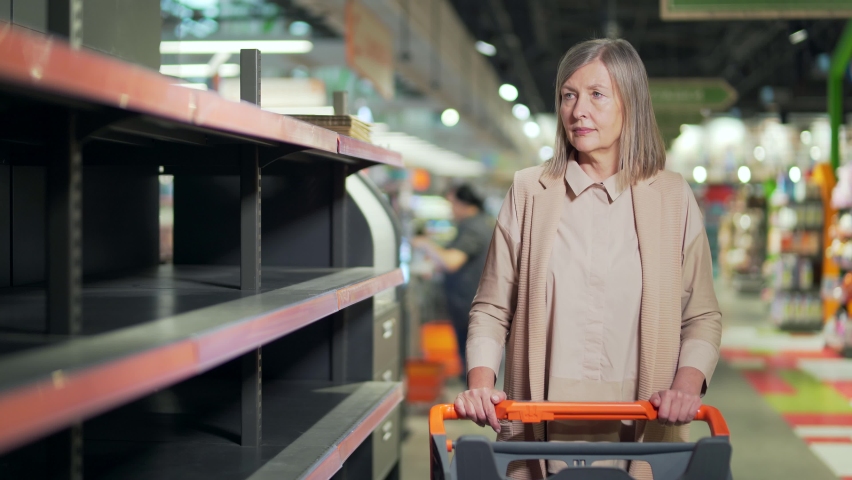 Senior woman shopper in supermarket, grocery store near empty shelves counters. Elder Mature female panic buying and stockpiling. groceries supplies with sold out products. Food supplies shortage Royalty-Free Stock Footage #1090822953