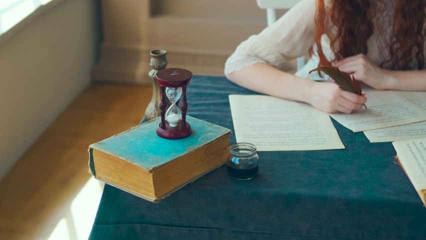 Medieval red-haired woman writer holds pen feather quill in hands close-up, face cropped, red hair. Girl sits at desk writes letter on sheet paper. Vintage dress, old books. student studying in room Royalty-Free Stock Footage #1090825445