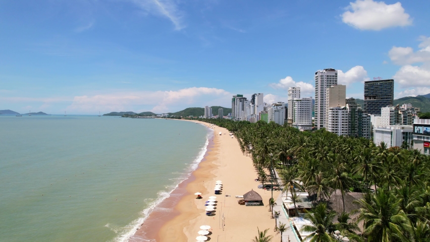 aerial drone flying center with the tropical white sand beach on a sunny day full of coconut trees and tall beachside hotels and beautiful turquoise ocean on the left side located in Nha Trang Vietnam Royalty-Free Stock Footage #1090825641