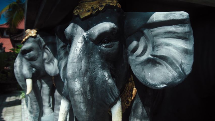 Statues of elephants in hats holding a concrete slab on their backs