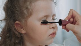 Mom does her five-year-old daughter's makeup before a party. A parent applies mascara to her little girl. Baby is putting on beauty, imitating the adults. High quality 4k footage