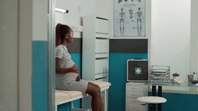 Portrait of african american pregnant woman in cabinet sitting on bed in medical cabinet. Patient with pregnancy belly and baby bump attending prenatal checkup visit appointment. - Powered by Shutterstock - Get 15% off with code: PIKWIZARD15