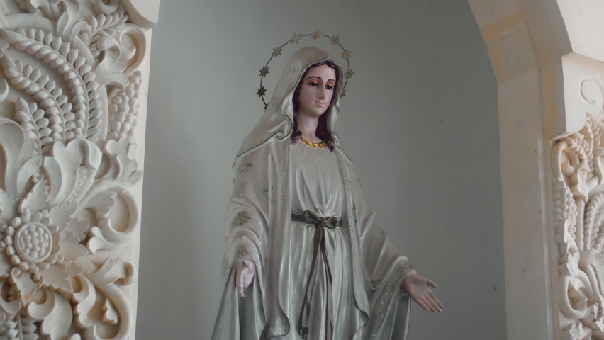 Statue of the Virgin Mary standing indoors with her head bowed looks straight Royalty-Free Stock Footage #1090832147