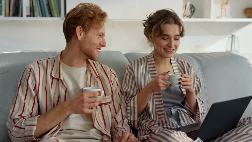 Young couple enjoy coffee on comfy couch closeup. Morning leisure time at home. Smiling beautiful family talking drinking beverages together on weekend. Relaxed girl ginger man laptop browsing web Royalty-Free Stock Footage #1090832349