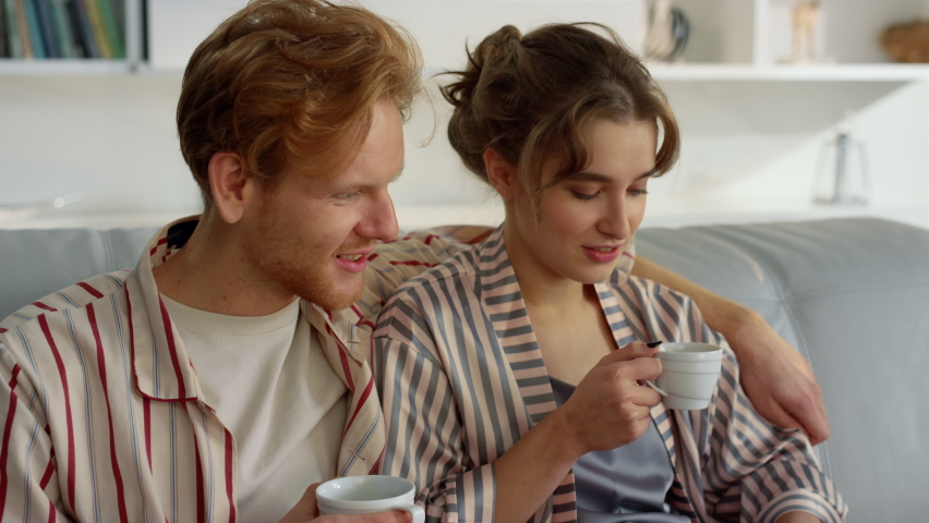 Joyful lovers watching laptop on comfy couch closeup. Romantic couple in morning drinking coffee. Happy ginger man embracing smiling wife browsing discussing vacation plan. Family lifestyle concept Royalty-Free Stock Footage #1090832353