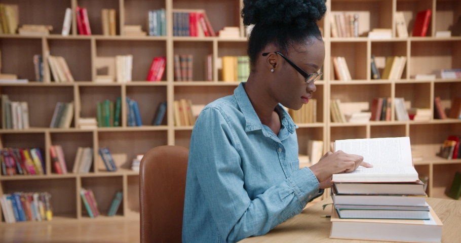 Young African American woman in glasses closes book and puts head down. Female student hides face from exhaustion and disappointment, while sitting in library. Royalty-Free Stock Footage #1090833409