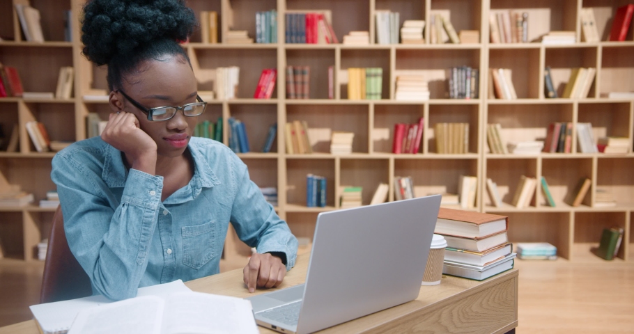 Young African American woman in glasses closes laptop and holds up help sign in front of face. Female student hides face from exhaustion and disappointment, while sitting in library. Royalty-Free Stock Footage #1090833411