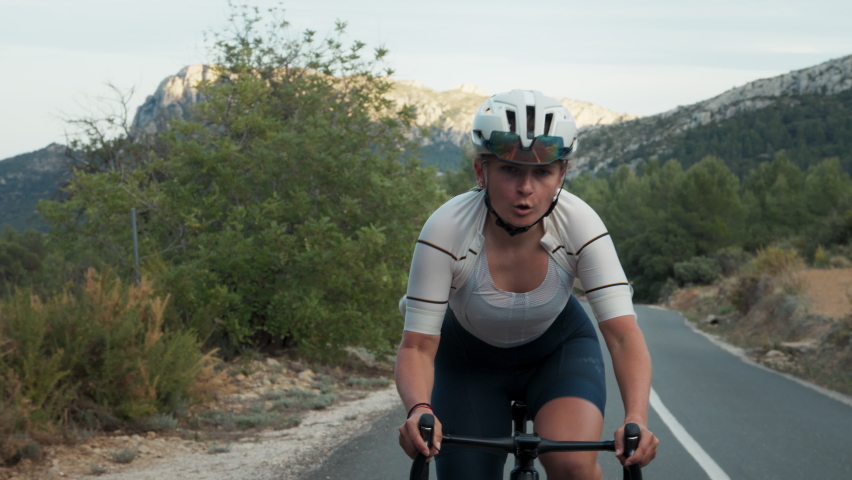 Close up of professional road cyclist, young pretty energetic woman rides bike on high mountain road on daily activity difficult sport intense hard training. Healthy outdoor lifestyle for athletes | Shutterstock HD Video #1090833627
