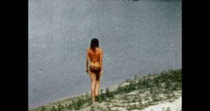 Woman in bikini walks on river beach at sunny summer. Beautiful model happy girl in swimsuit resting near lake water. Holiday vacation. Vintage color film. Retro 80s, 90s archive. 1980s-1990s. 4k