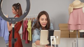 Beautiful asian woman blogger choose clothes in the clothes rail While one female in front of camera to recording vlog video live streaming at her shop. Business online influencer on social media.