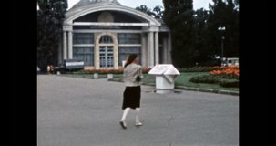 Woman walks along street in summer Kyiv. City center travel. Exhibition Center VDNH in soviet Ukraine. Green trees in park. Vintage color film. Old scanned historic archive. Retro 1980s 4K footage