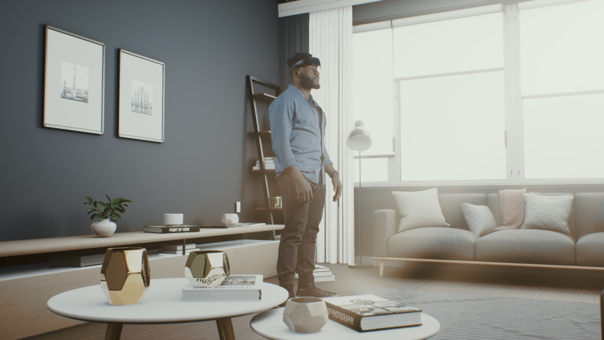 A man at home puts on a virtual reality headset and connects to the cyber space metaverse in which he is like an avatar and icons and interfaces of social networks, media surround him. Royalty-Free Stock Footage #1090841883