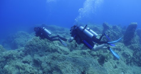  scuba diver exploring around a reef underwater deep blue water big rocks and bubbles ocean scenery