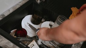 Housework. Cleaning. Man washes dirty dishes. Plates, cups, glasses, spoons, forks are in the sink. A man with a sponge with a soap solution washes kitchen utensils. Soft focus. time lapse - Powered by Shutterstock - Get 15% off with code: PIKWIZARD15