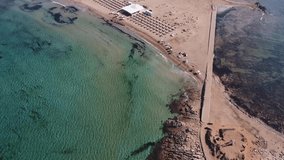 Aerial drone footage of the island and beach of Isola delle Correnti with an old lighthouse surrounded by clear turquoise sea water. Southernmost point in Sicily, Portopalo di Capo Passero, Italy.