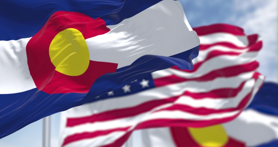 Seamless loop in slow motion with two flags of the Colorado state waving along with the national flag of the United States of America. In the background there is a clear sky. Royalty-Free Stock Footage #1090845091