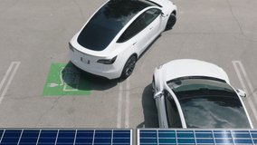 Generic electric car driving by city parking lot parking at electric vehicle charging station under blue solar panel batteries. Zero emission vehicle on EV only charging station on sunny summer day 4K - Powered by Shutterstock - Get 15% off with code: PIKWIZARD15